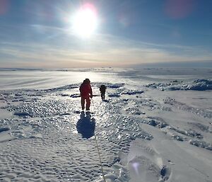 Two people walk across an icy glacier.
