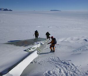 Three expeditioners stand next to the remnants of an aircraft wing
