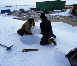 Two men cut ice blocks from an ice embankment.