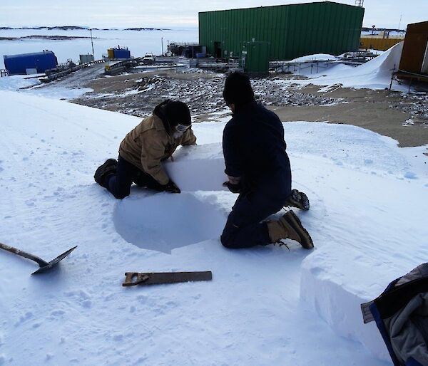 Two men cut ice blocks from an ice embankment.