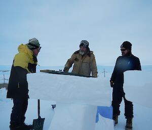 Three men stand outside in front of pillars of ice.