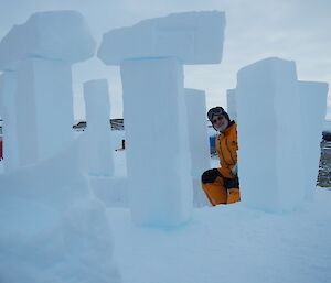 A man in a yellow freezer suits sits next to an ice pillar