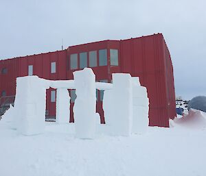 A circle of ice pillars are positioned on an ice bank in front of a red shed.