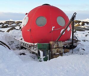 A red domed hut on a wooden stand in the snow.