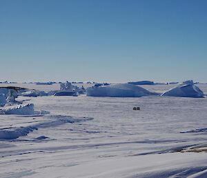 A frozen landscape with icebergs and a yellow Hägglunds is in the foreground