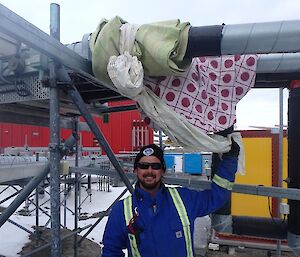 A man stands in front of pipes wrapped in sheets and blankets