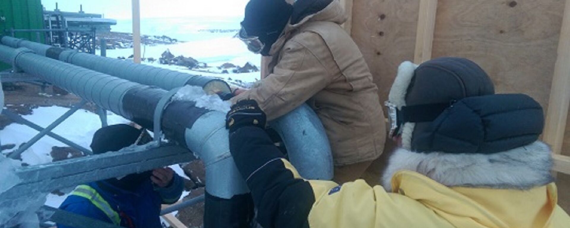 Three men work on a pump outside.