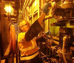 A man in high visibility uniform is repairing a pump inside a tank house.