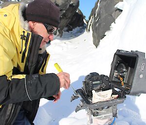 A man holds a screw driver in front of an open camera box.