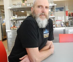 A man with a grey beard sits at a table.