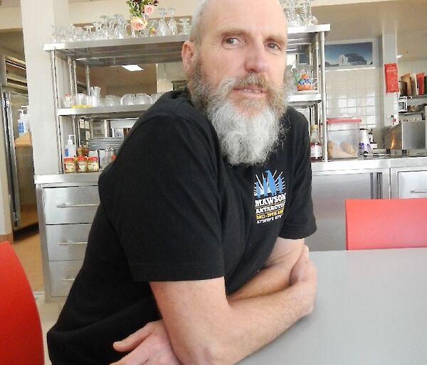 A man with a grey beard sits at a table.