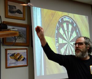 A man shoots a dart with a dart board image in the background