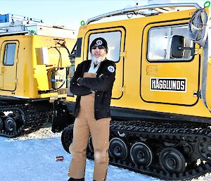 A man wearing sunglasses and a beanie stands in front of a yellow Hägglunds