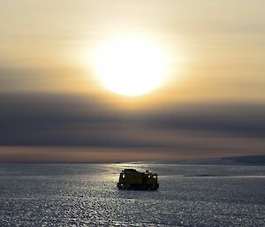 A Hägglunds vehicle is on an icy plateau at sunrise.