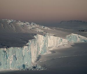 A blue and white ice cliff edge with a pink sunrise.