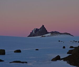 A pink sunset over an ice plateau and Nunatak mountain peaks