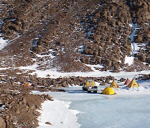 A polar campsite of yellow tents at the base of a rocky mountain