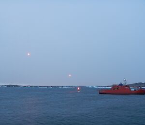 A red ship sails away followed by orange flares in the sky