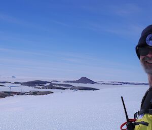 A man wearing a beanie and sunglasses smiles at the camera standing on an icy plateau.