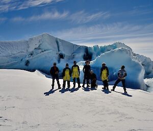 Seven people stand in front of a snow covered jade berg.