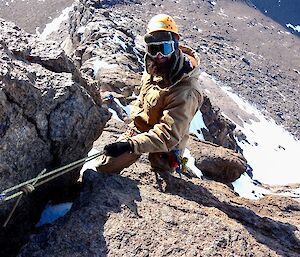 A man holds on to a rope climbing up a rock face.