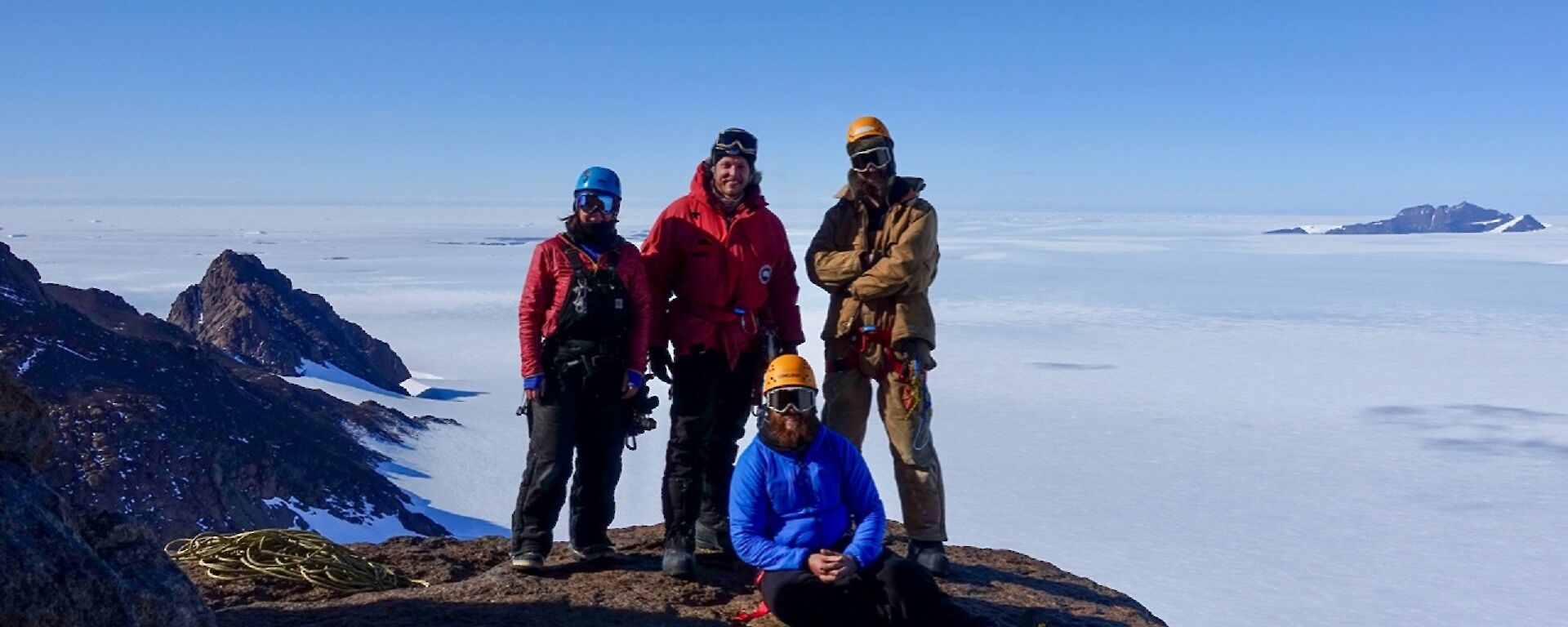 Four people stand on a rock ledge with a plateau behind them.