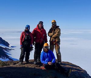 Four people stand on a rock ledge with a plateau behind them.