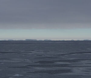 A grey sea with icebergs and the Antarctic ice sheet on the horizon