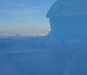 A bright blue iceberg in the foreground with a sun lit horizon of icebergs in the distance.
