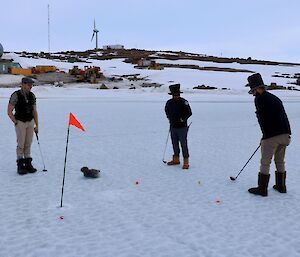 Two men watch a man lining up a golf shot standing on sea ice