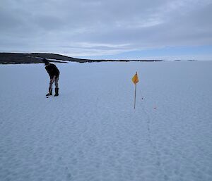 A man stands on sea ice aiming a golf ball at the flag