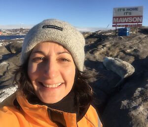 a woman wearing a beanie stands in front of a sign that says ‘It’s home, It’s Mawson.'