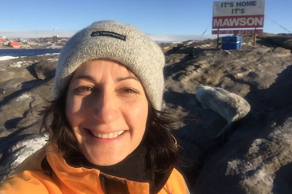 a woman wearing a beanie stands in front of a sign that says ‘It’s home, It’s Mawson.'