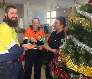 Three men stand next to a Christmas tree holding bon bon crackers.