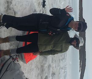 Two women stand next to sleds on the sea ice.