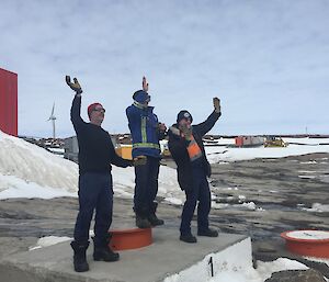 Three men stand on a bollard waving their arms.