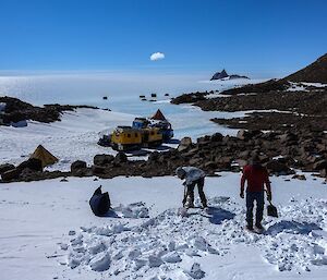 3 people moving snow in preparation for putting up a tent.