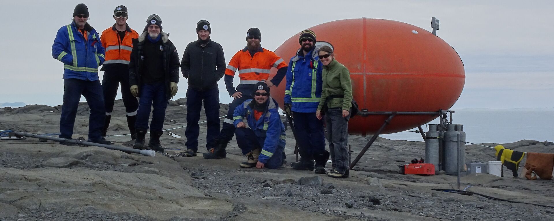 A group of people stand in front of a googie hut on Bechervaise Island