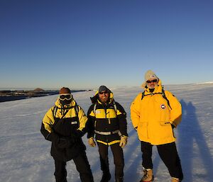 3 men pose for a photo on the ice plateau with open sea visible behind them