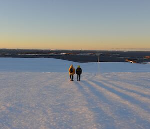 2 men walk away from camera towards the coast