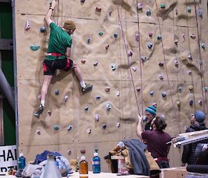 A man on a climbing wall with 3 people on the ground