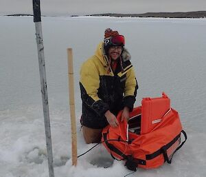 A man kneeling on the sea ice smiles at camera