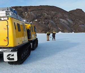 2 men stand on the ice plateau with a Hägglunds vehicle