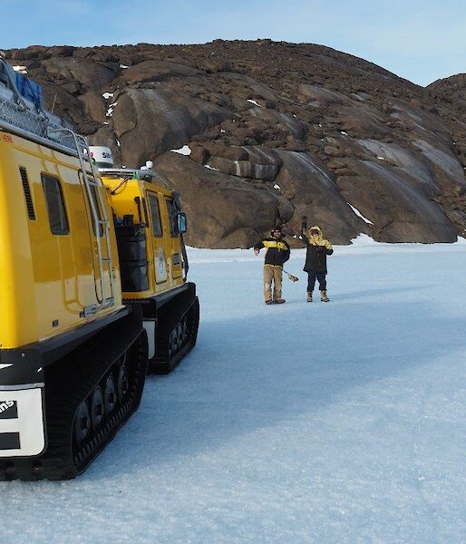2 men stand on the ice plateau with a Hägglunds vehicle