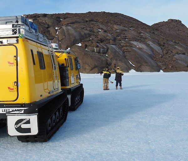 2 men stand on the ice plateau with a Hägglunds vehicle