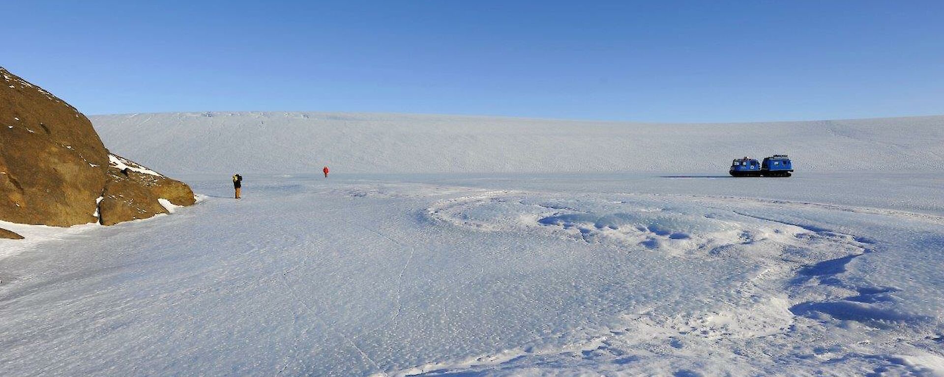 A vehicle and 2 people out on the ice