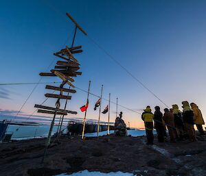A group of people around flag poles and Mawson station at dawn