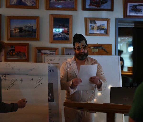 A man dressed as Elvis watches a man drawing