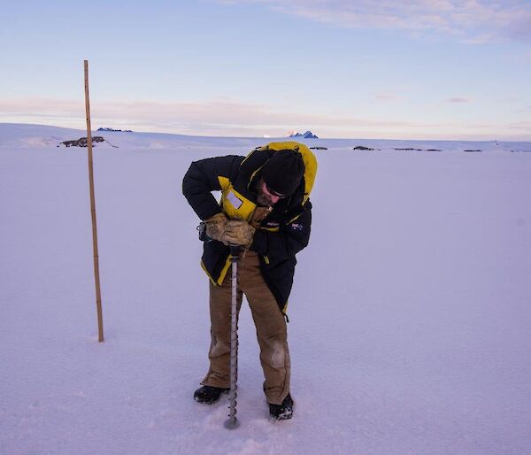A man drills a hole in the sea ice