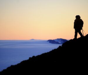 A man in shadow walking the ridge line at sunset